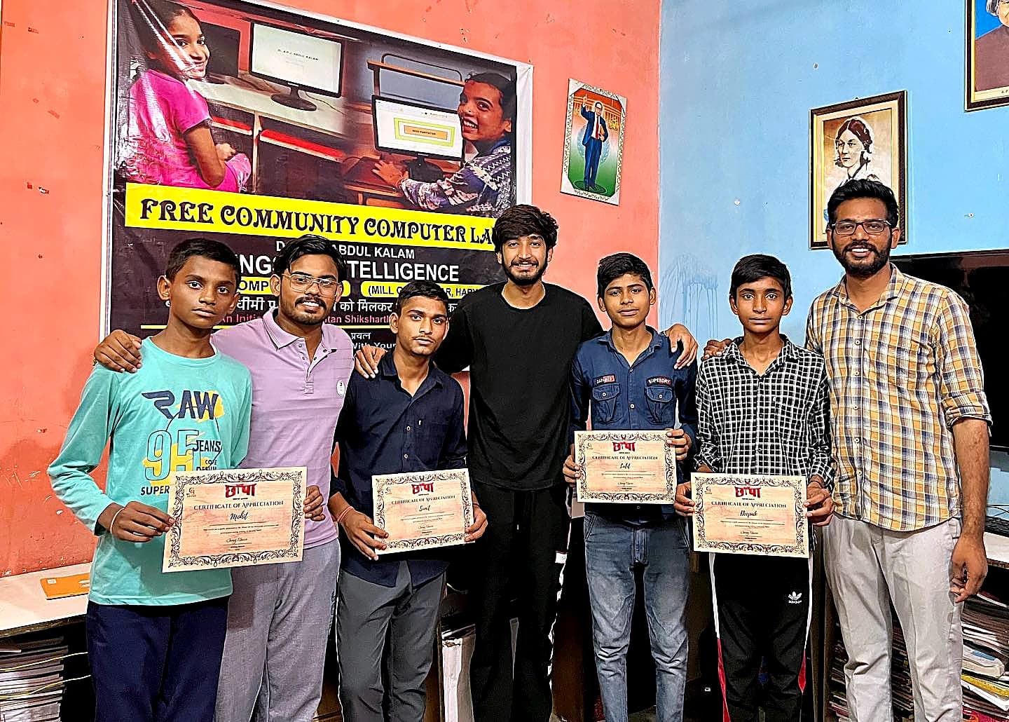Four students of the Free Community Computer Lab holding certificates of appreciation with their mentors, under the lab banner in Hisar