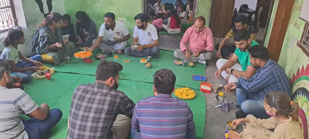 Mentors and students eating the same food seated in one row on the floor